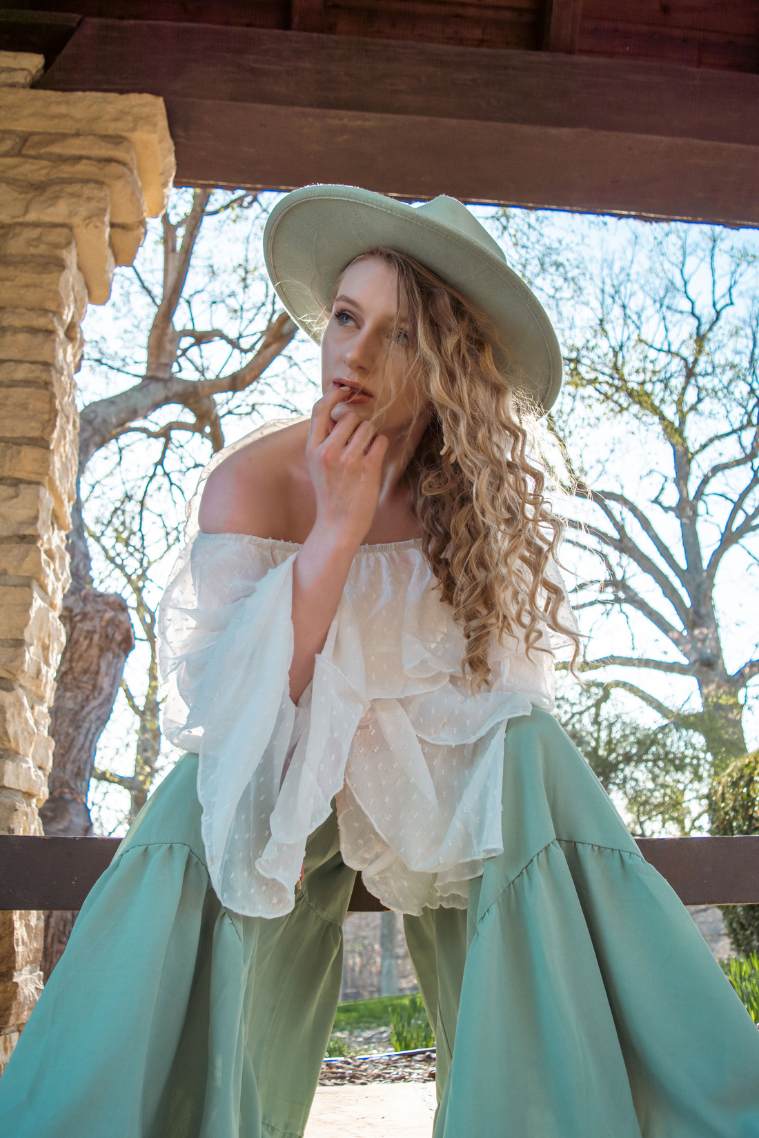 Woman Wearing a White Flowing Top with Wide Legged Sage Green Pants and A Sage Green Fedora Hat